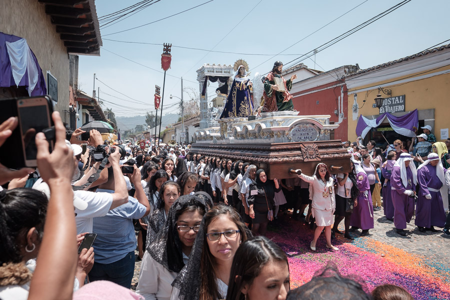 Through the smoke, a float is marched step by step down the center of the avenue. Onlookers watch the scene respectfully and emotionally.