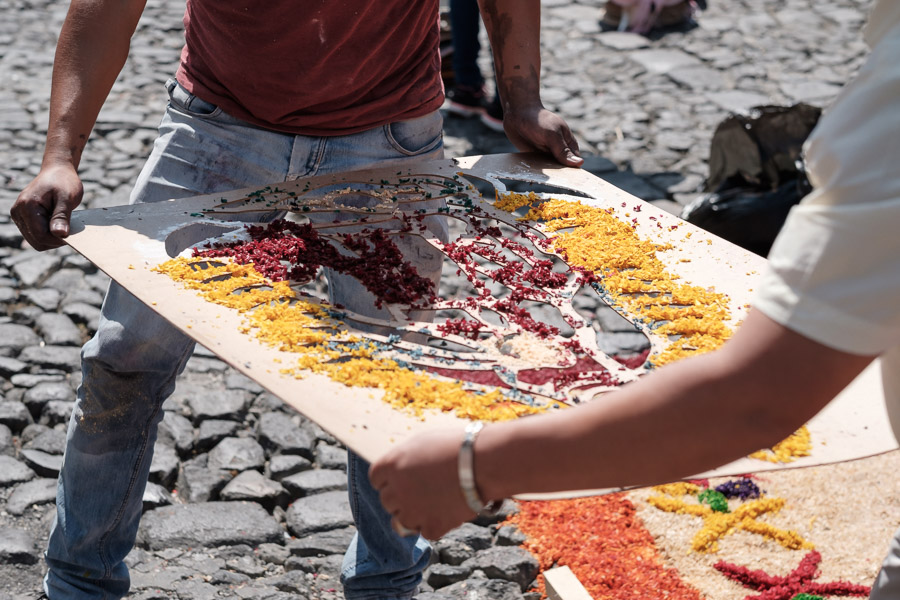 Vibrant sawdust slips through the holes of a homemade stencil, creating a detailed depiction of the Virgin Mary.