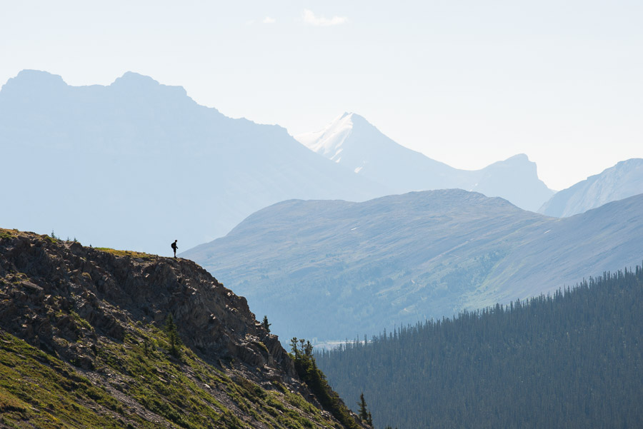 A lone hiker is silhouetted against a hazy mountain ridge as he climbs above the tree line.