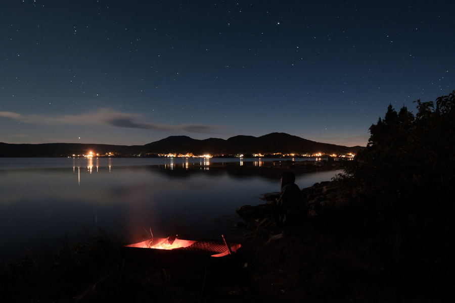 Lights of both the old and modern sort light up an otherwise dark ocean inlet.