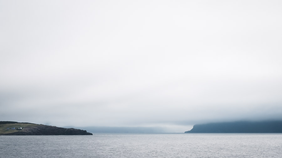 Small homes seemingly cling to rugged shore, dwarfed by both land and weather.