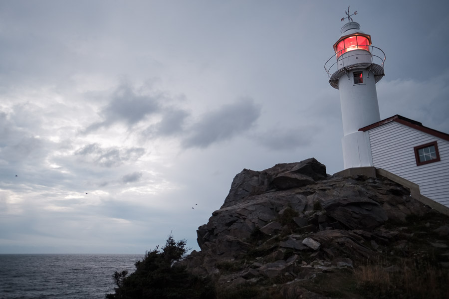 A lighthouse shines bright against a darkening sky; both night and an approaching storm are on the horizon.