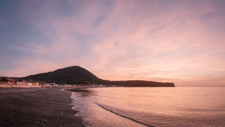 The sun sets and moon rises over a seaside town on the westerly shore.