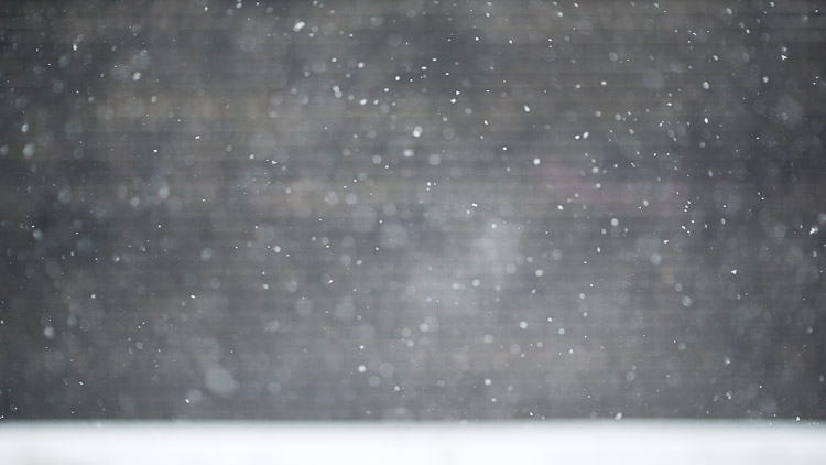 Heavy snowflakes drifting past a dark blurred wall during a spring snowstorm
