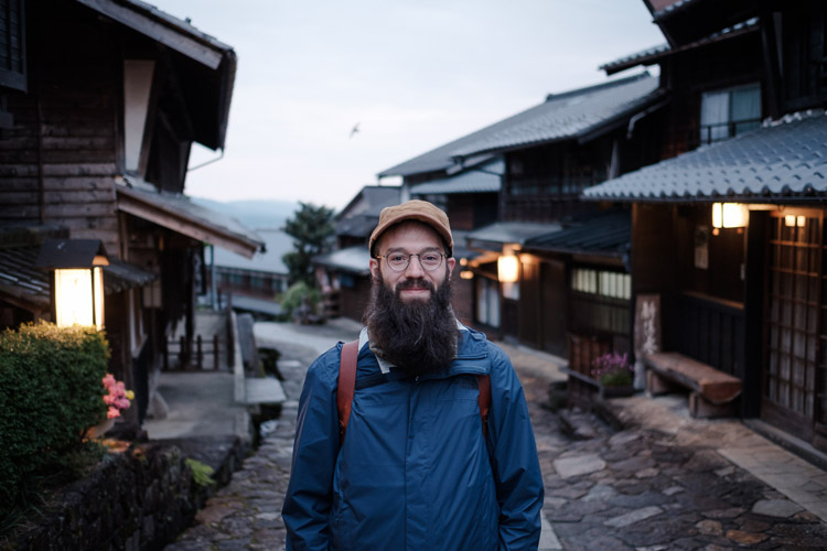 David stands smiling on the stone-paved street of Magome at dusk, lantern-lit wooden inns lining the old post town