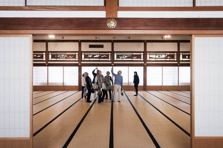 Visitors stand in a vast tatami hall at Eiheiji Temple, gazing up between sliding paper doors and carved wooden transoms