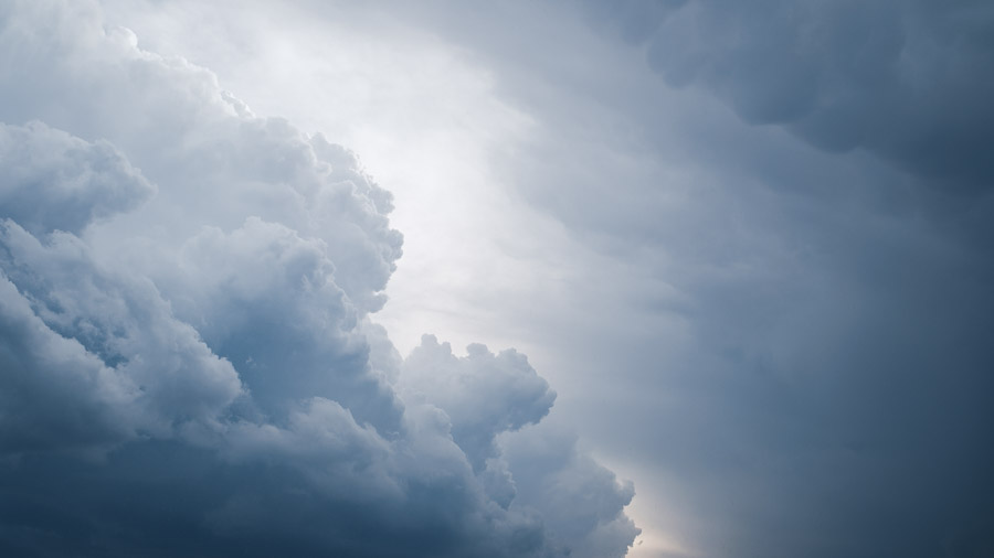 Towering blue-grey storm clouds billowing upward, backlit by the sun