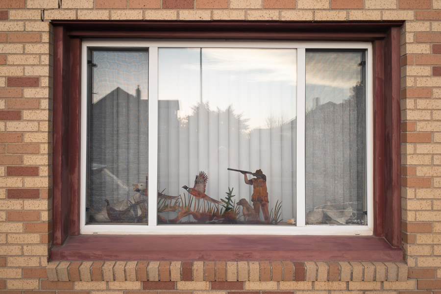Cutout figures of a hunter, pheasant, and dog arranged in the picture window of a brick house in North Dakota