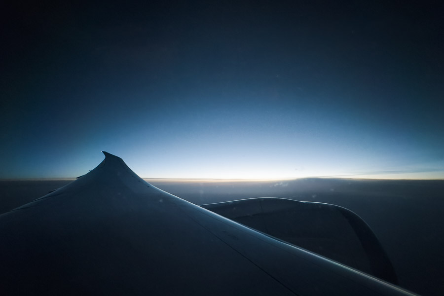 An airplane wing and engine silhouetted against the last blue-orange glow of the horizon at cruising altitude