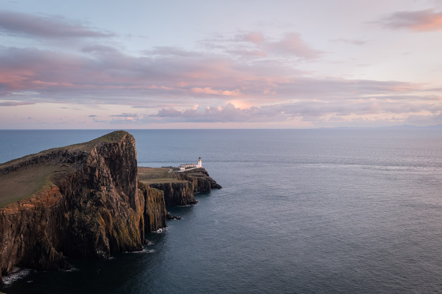 Neist Point lighthouse perched at the tip of sea cliffs under pink sunset clouds on the Isle of Skye